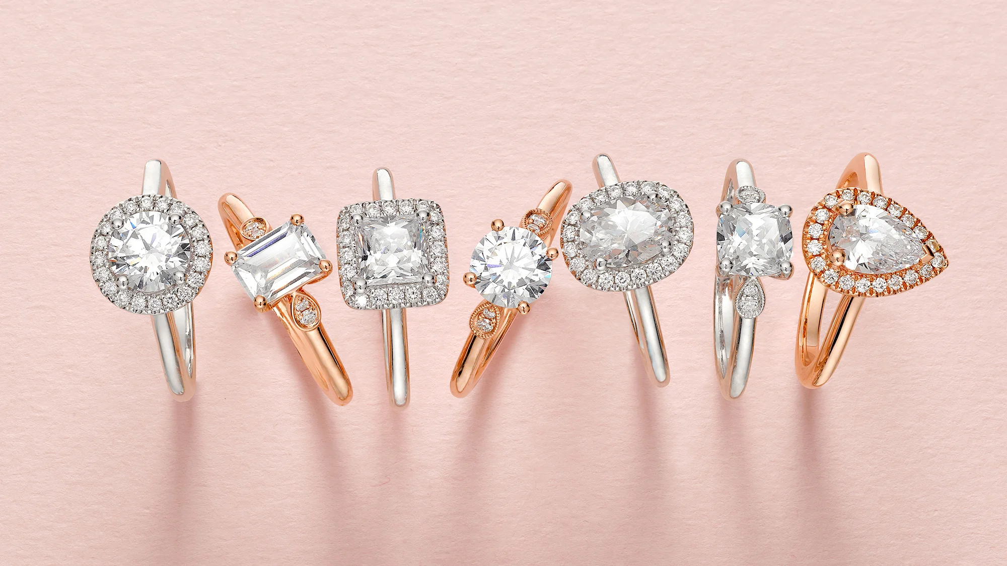Diamond rings in silver and rose-gold tones arranged on a pink background