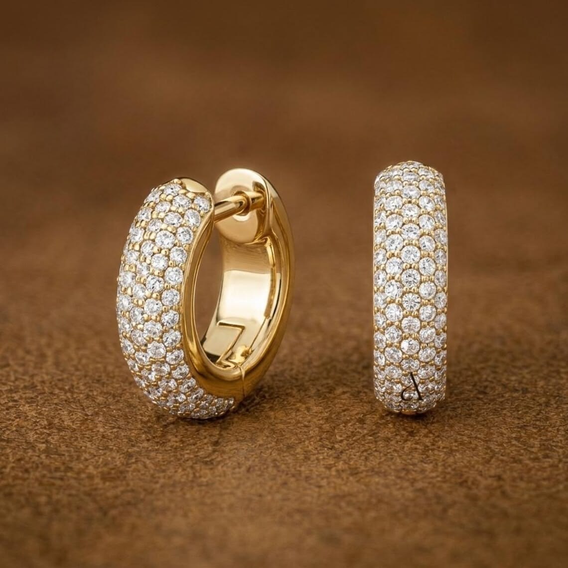 Gold hoop earrings set with rows of diamonds on a warm brown background