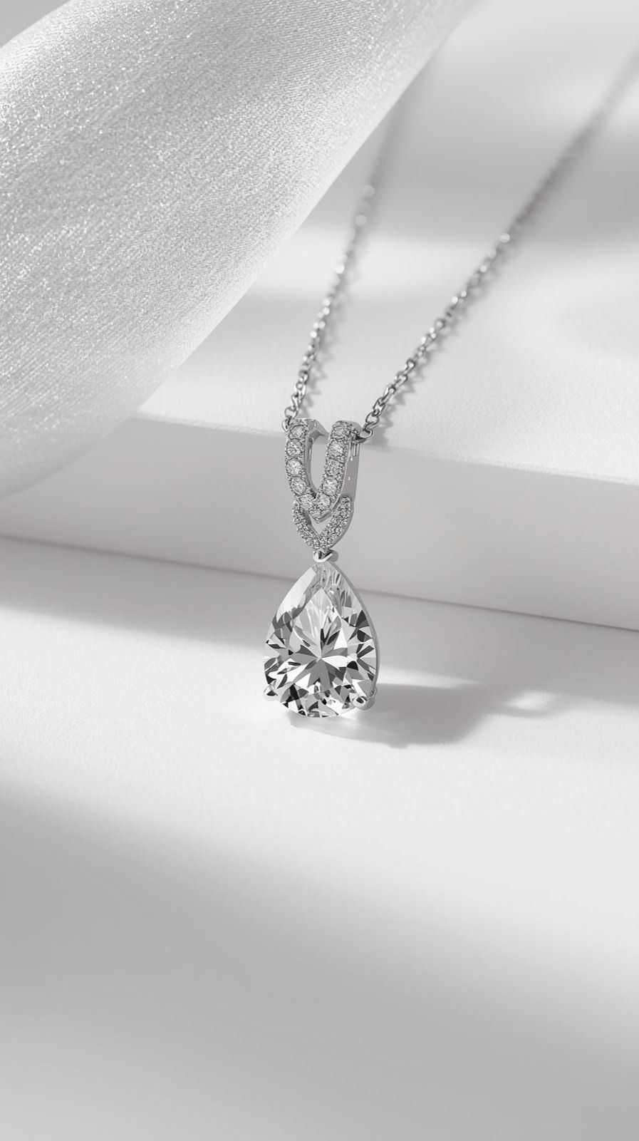 A pear-shaped diamond pendant and silver chain resting on white fabric